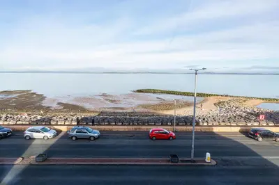 a parking lot with cars parked next to the water at Stylish Seafront Apartment - Sleeps 6 - Gateway to the Lakes in Morecambe