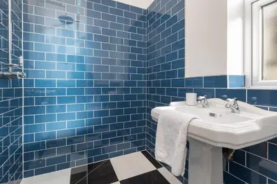 a blue tiled bathroom with a sink and a mirror at Ettie's in Blackpool