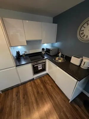 a kitchen with white cabinets and a clock on the wall at Stunning City View Studio Apartment by StaySavvy Accommodation in Liverpool