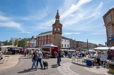a group of people walking around a market with a clock tower at Sleeps 10 Spacious for Contractors by PolkaStay in Ormskirk